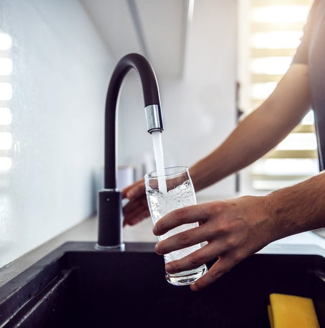 Close up of young man pouring fresh water from kitchen sink